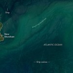 In the blue-green ocean a small island sits to the left portion of the image. The green island is outlined with a bright somewhat yellow border of beach and has an inland pond connected to the ocean.